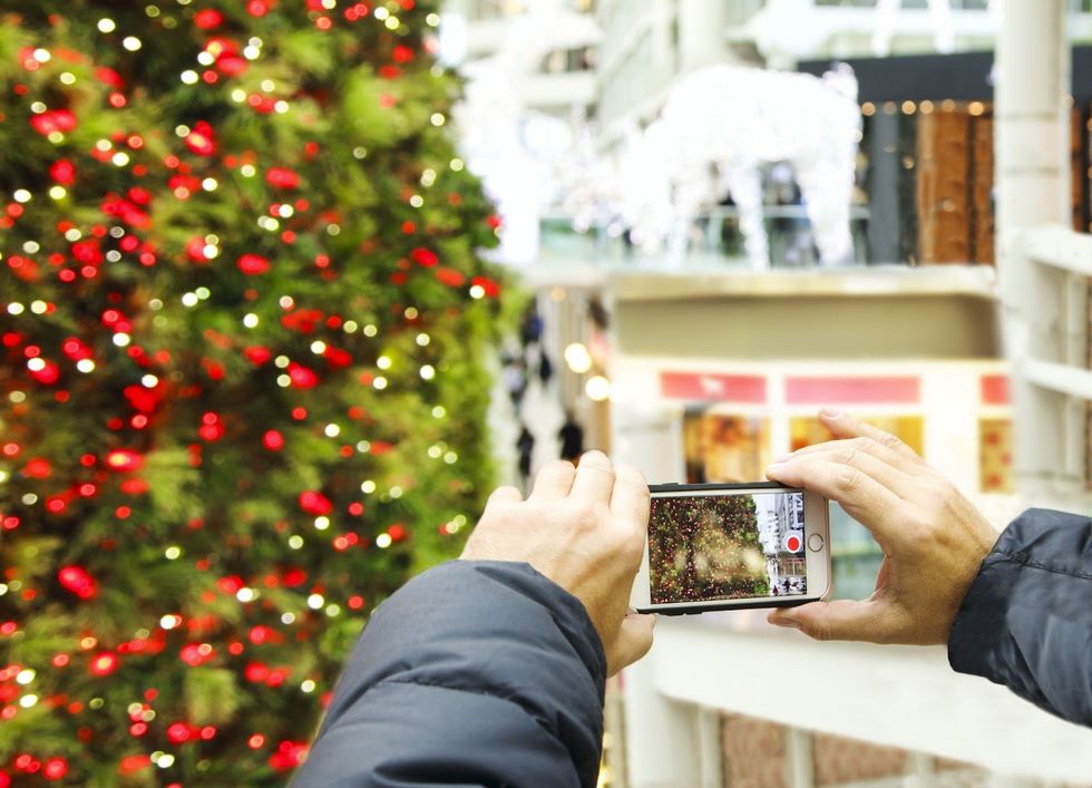 A close up of a person's hands holding a phone as they take a photo of the holiday tree at CF Toronto Eaton Centre.