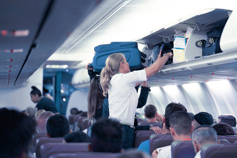 Flight attendant stowing luggage.