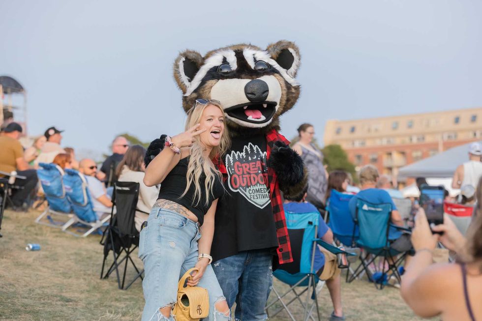 A Great Outdoors Comedy Festival guest poses with the racoon mascot.