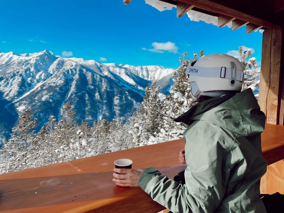 Morgan Leet holding a drink at Elkhorn Cabin with the mountains behind her