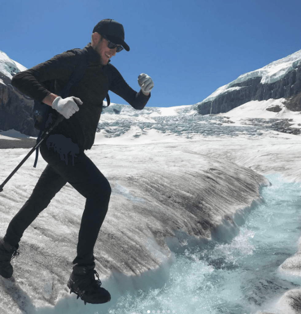 A man jumps over a river of melting glacial water.
