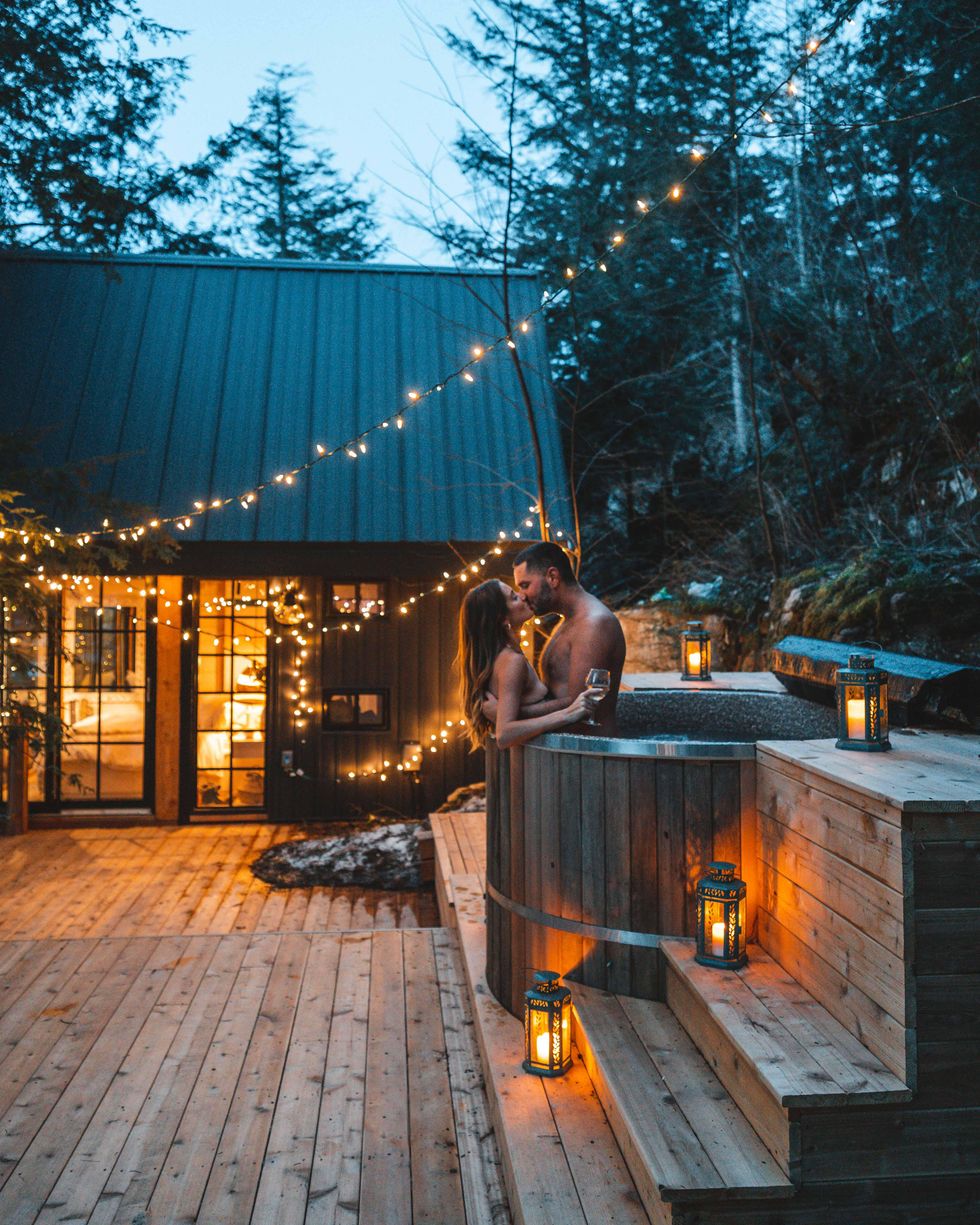 Couple kissing in a hot tub surrounded by lights and lanterns in Muskoka.