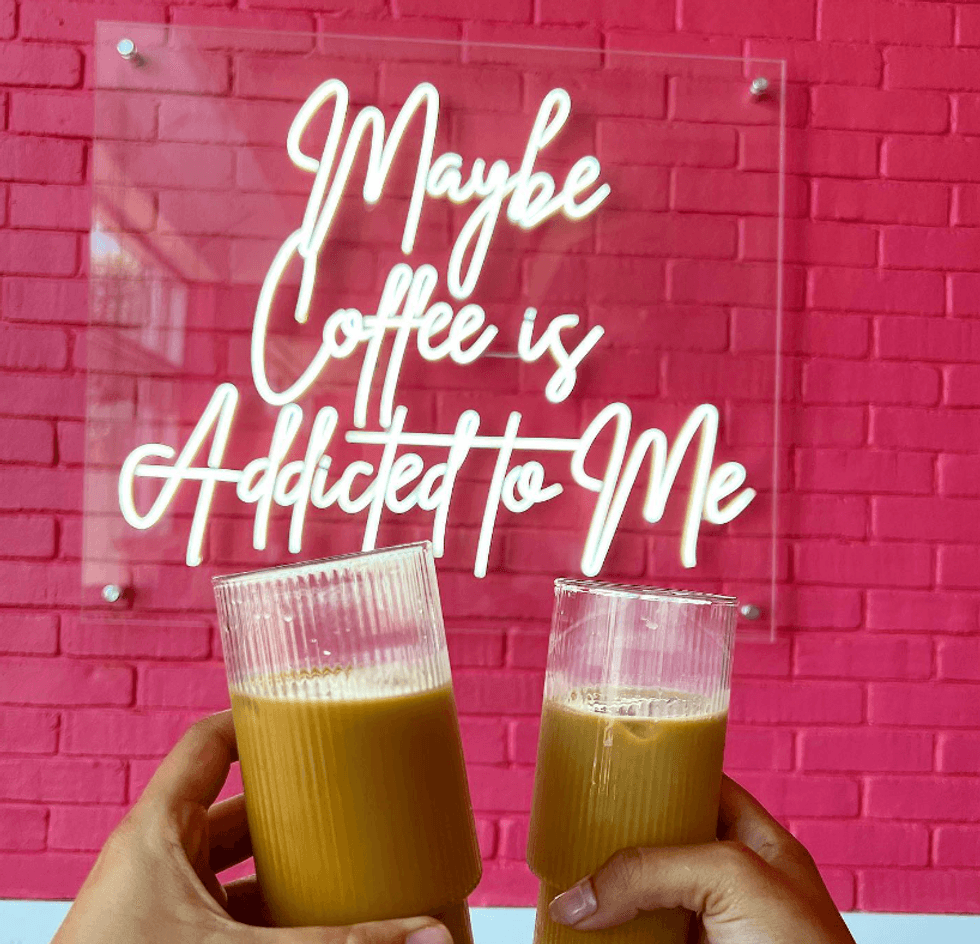 Hands holding coffee in front of a neon sign.