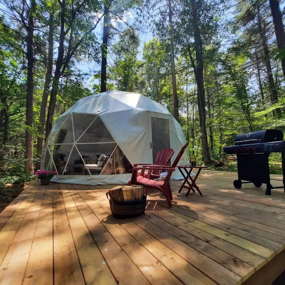 Wooden deck off of a dome Airbnb with chairs, wood for burning and a BBQ.