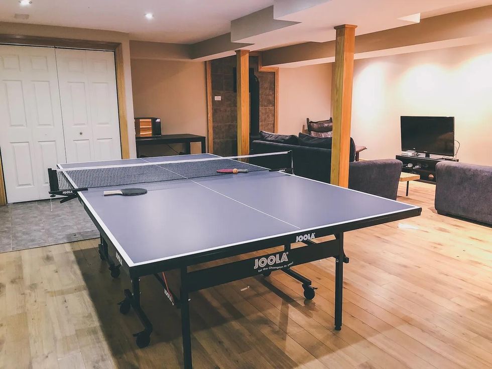 Basement living room of large Ontario cabin with a ping pong table and wood burning stove.