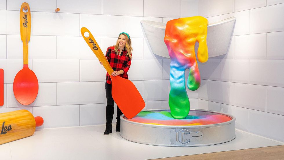 Woman standing with giant baking utensils.